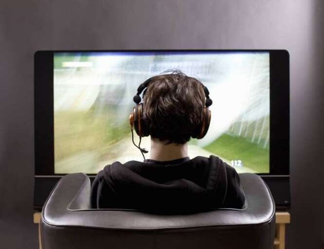 Teenage boy sits in front of TV playing video game