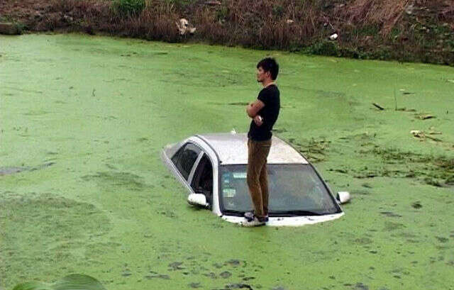 Homem fica de pé em cima de seu carro submerso em lagoa